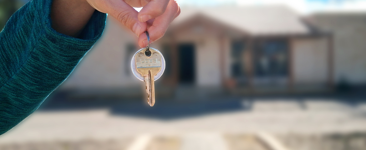 close up of keys in front of sold house